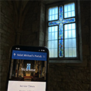 I'mage of a phone with a church website on it, with a stained glass window in the background in the shape of a cross.
